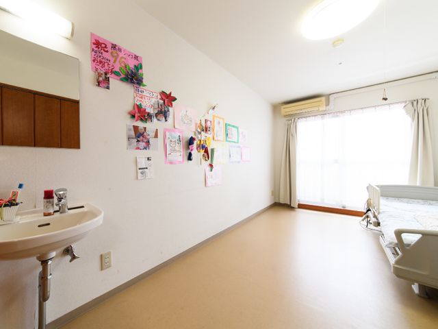 明るく広々とした居室 居室 居室にはベッドと洗面台があり、壁には様々な掲示物が飾られております。掲示物には利用者の個性が表れ、温かみのある雰囲気を感じさせます。