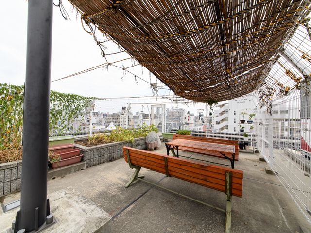 屋上テラスと休憩中の人 屋上 屋上に設けられたテラスで、一人の方がベンチでゆったりと休憩されています。都会を眺めながらのひとときをお過ごしいただける空間です。
