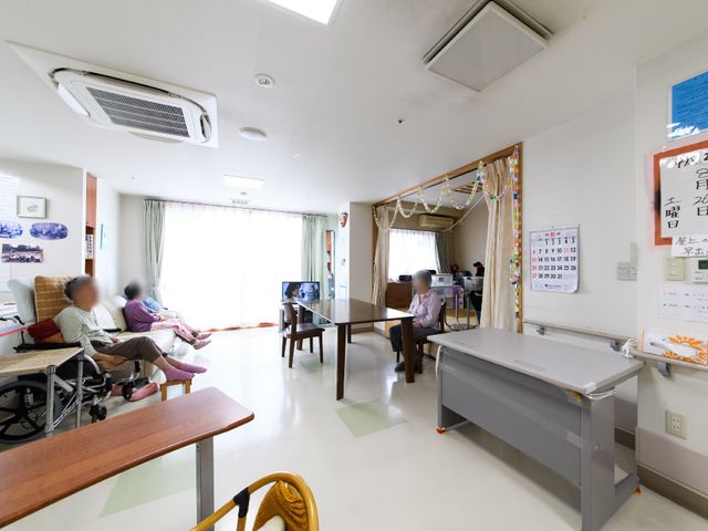 居室内でくつろぐ人々 部屋 ゆったりとしたリビングで、入居者がテレビを楽しみながらくつろいでいます。明るく開放感のある空間で、心地よい時を過ごせる場所です。