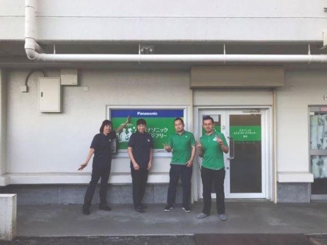 スタッフが並ぶ建物外観 外観   建物の前で4人のスタッフの方が並んでいます。出入口まわりが見え、職場の雰囲気を感じやすい外まわりです。