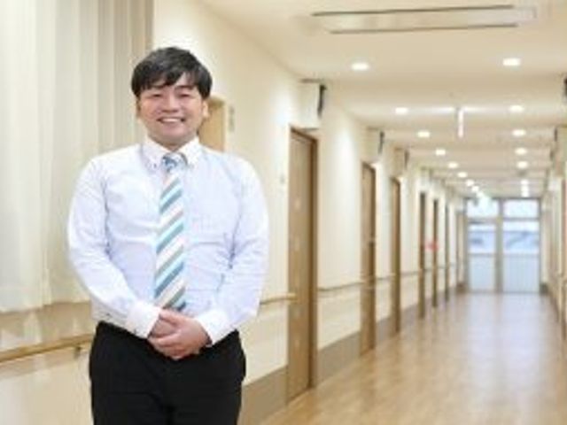 スタッフと廊下 笑顔で立つスタッフが印象的な明るく清潔な廊下です。ゆったりとしたスペースで快適な移動を支えています。