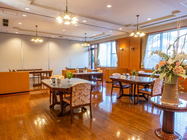 落ち着いた雰囲気の食堂 ダイニングルーム 広々とした食堂は温もりある木のテーブルが並び、大きな窓から自然光が差し込んでいます。装飾されたフラワーアレンジメントが上品な印象を与えています。