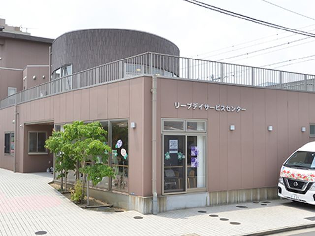広々とした建物と車 外観 周辺に花柄の車が並ぶ、開放的で親しみやすい建物です。働く環境が気持ちよく整っています。