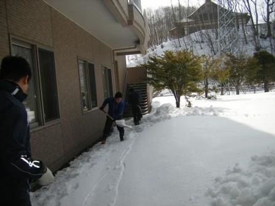 雪かきする職員と建物外観  