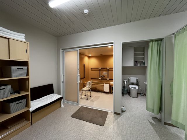 明るい個室と浴室 居室   収納棚やベッドが備わった落ち着いた個室です。奥に浴室とトイレがあり、使いやすさが伝わります。
