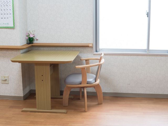 清潔な居室の一角 共有スペース 窓辺に置かれた机と椅子が、明るく穏やかなひとときをお過ごしいただける空間を作り出しております。壁にはカレンダーも掲げられ、日々の生活に役立てていただけます。
