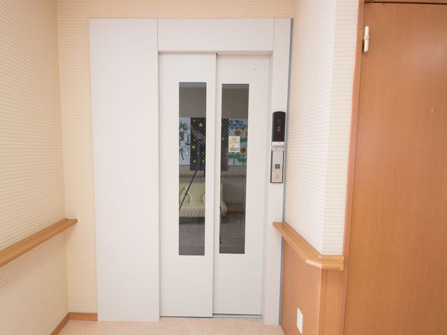 エレベーター付近の廊下 エレベーター 手すり付きの廊下が続き、エレベーターの前には待合いスペースが確保されています。利用者の動線を考えた配慮が行き届いています。