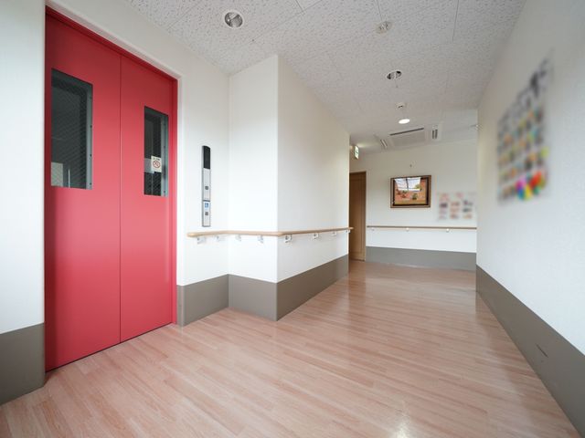 赤いドアのある廊下 通路 広々とした清潔感のある廊下が確保されており、安全な手すりも設置されています。ゆったりとした空間で働ける環境が整っています。