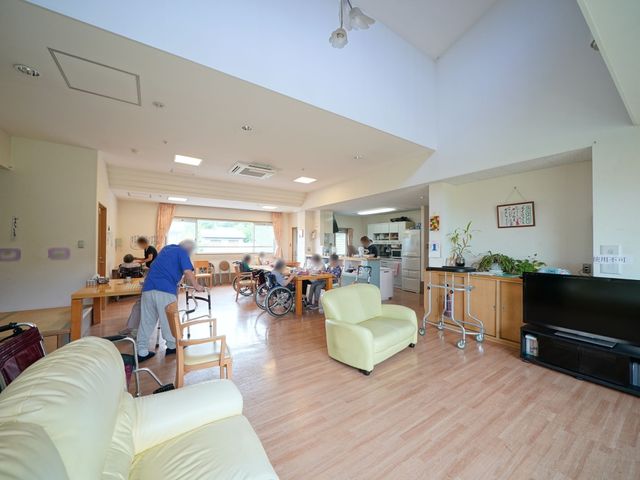 共用スペースの日常風景 共有スペース 座椅子に座って対話を楽しむ方々、キッチンで調理をするスタッフの姿が見え、活気に満ちた憩いの場が広がっています。明るく開放的なリビングで、共に働く喜びを感じてみませんか。
