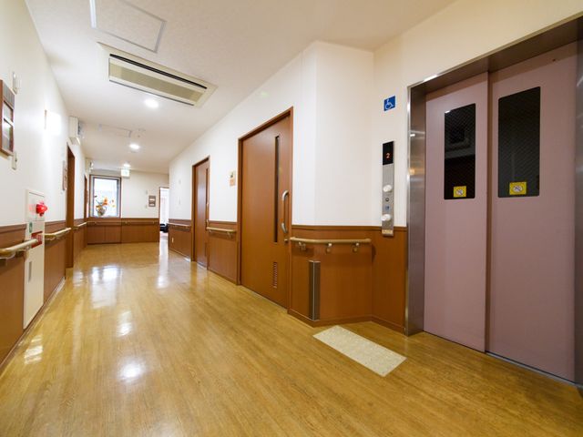 明るい施設の廊下 エレベーター 床が輝く清潔感のあふれる廊下が、訪れる方を暖かく迎えます。車椅子の方も安心して移動できる広々とした空間です。