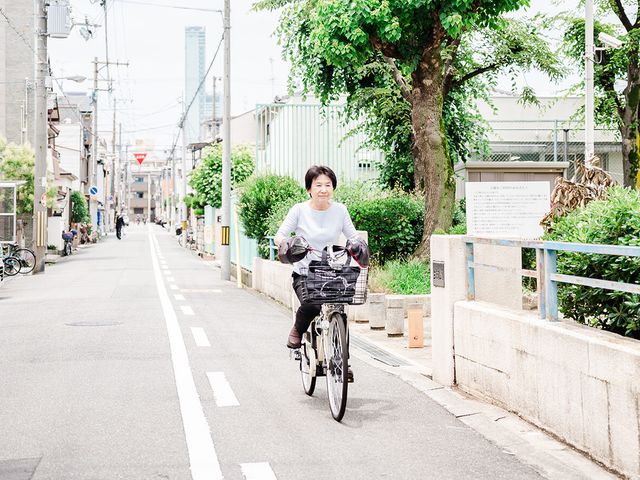 道を進む自転車の人 外観 都市の風景の中、自転車で移動する女性が見られます。周囲には木々が茂っています。