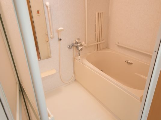 白で統一された爽やかな浴室にはバスタブとシャワー、鏡が設置されている。また、手すりが各所に取りつけられている。