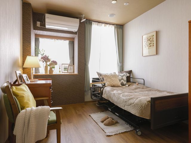 居室の明るいインテリア 一人部屋 床材が明るく、窓際には植物が置かれた快適な空間です。ゆったりとした時間を過ごせそうな椅子もあります。