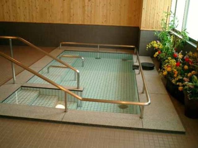 温もりある浴室空間 大浴場 手すり付きの広々とした浴室は、清潔感があり、花々が彩りを添えて温かな雰囲気を演出しています。