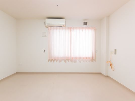 施設の写真 白を基調としたシンプルなデザインの居室である。エアコンが完備されている。壁には緊急連絡用のボタンがある。