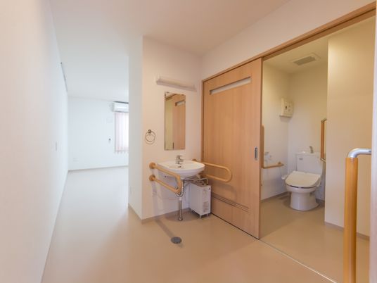 施設の写真 トイレ内は広く、車椅子でも入ることができる。扉は引き戸で大きく開くようになっている。トイレ内や洗面台には手すりが設置されている。