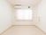 サムネイル 施設の写真 白色で揃えた清潔感のある居室。エアコンがある。長いコード付きの緊急用ボタンが壁に備え付けてある。