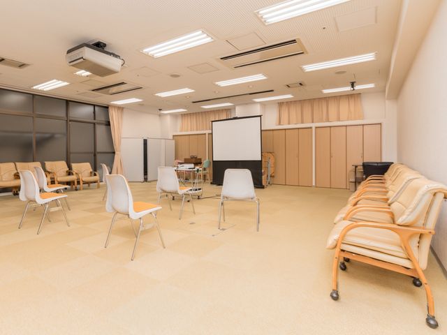広々とした多目的スペース 多目的ホール 広々とした室内空間は、入居者が様々な活動を楽しめるように整えられています。ゆったりとした椅子が配置され、快適なコミュニケーションの場を提供します。