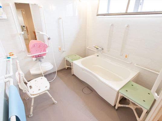 浴室には大きな窓がある。浴槽周囲に介護用の椅子が設置され、洗い場にも椅子が１脚ある。壁に手すりが取りつけられている。