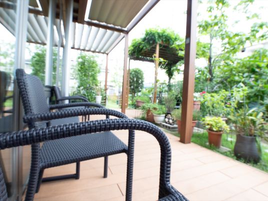 中庭に面したテラスがある。１人掛けの黒い椅子が窓際に並べられている。中庭には鉢植えや樹木などが育てられている。