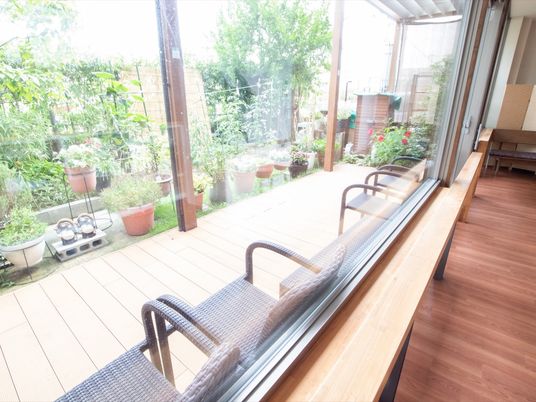 共有スペースの大きな窓の外にテラスがあり、窓際に１人掛けの椅子が並べられている。広い中庭を眺めることができる。