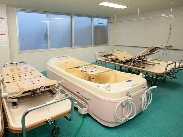 入浴設備が並ぶ浴室 浴室   機械浴槽と移乗用ベッドが配置された浴室です。広い作業スペースがあり、介助しやすい環境に見えます。