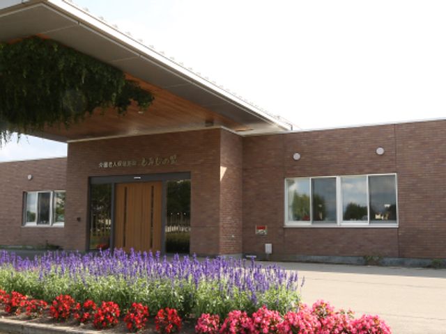 花に囲まれた建物エントランス 外観 色とりどりの花に囲まれた建物の外観です。明るく親しみやすい雰囲気が漂います。