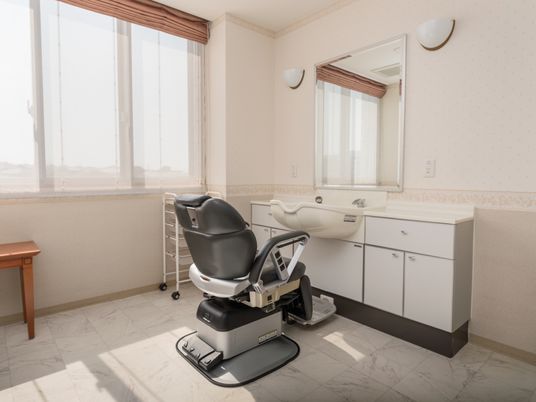 施設の写真 白を基調とした、日差しのたっぷり入る空間である。洗面台と大きな鏡の前には、ひじ掛け付きの椅子が設置されている。