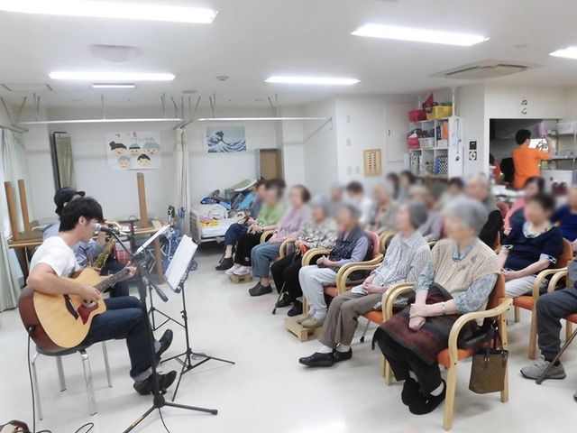 集まりを楽しむ部屋 ラウンジ 椅子に座った方々がギター演奏を楽しんでいます。和やかな雰囲気が漂う交流の場です。