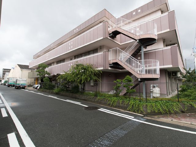 ピンクの建物の外観 施設の外観 ほっと一息つける外観のケアハウスです。植物に囲まれたエントランスが、訪れる人に安らぎを与えます。