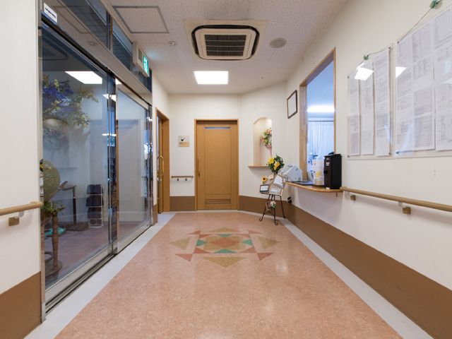 廊下に手すりと掲示物 機能訓練室から見える廊下 手すりが設けられ、ゆったりとした通路は歩行の安全をサポートします。掲示物も見やすい位置に配置されており、情報共有に配慮されています。