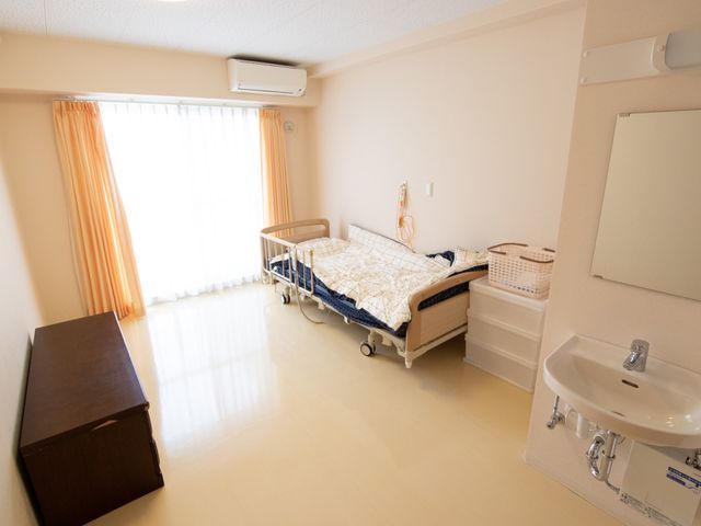居室のベッドと洗面台 居室 ゆとりを持った個室で、出窓から自然光が差し込んでいます。洗面台も備えており、日々の生活に必要な設備が整っています。