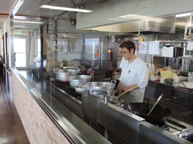 料理中のスタッフと厨房 台所 清潔感のあるキッチンで調理を行うスタッフの姿があります。こちらで、毎日の食事が心を込めて作られる様子をご覧いただけます。