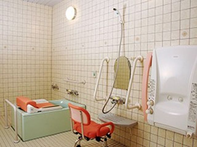 浴室の入浴設備 浴室   広い浴槽のそばに手すりやシャワー設備が整い、移乗用のイスも見えます。安全に配慮した入浴環境がうかがえます。