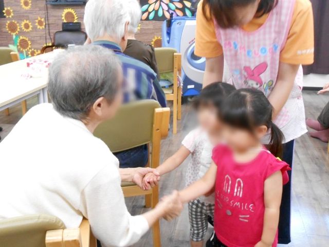 和やかな交流のダイニングルーム ダイニングルーム 笑顔で手をつなぐ高齢者とお子さん。お食事やコミュニケーションを楽しむ明るいダイニングルームです。