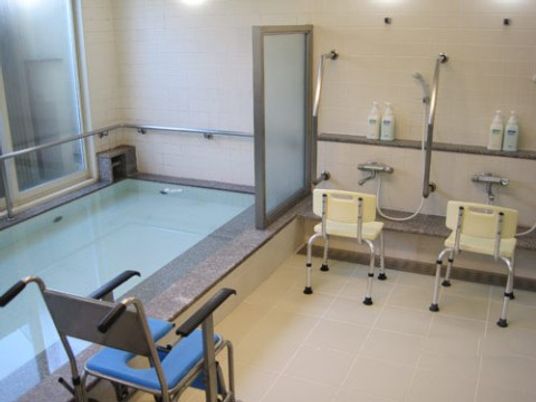 施設の写真 大きな浴槽が備え付けられた浴室となっている。シャワーの前にはシャワーベンチが置かれ、シャワー用車椅子も用意されている。