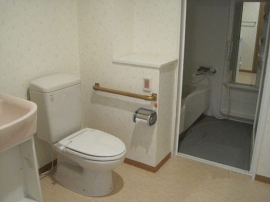 施設の写真 浴室の手前には、手すりと呼び出しボタンが備え付けられたトイレがある。車椅子に座ったまま使用することができる洗面台も用意されている。