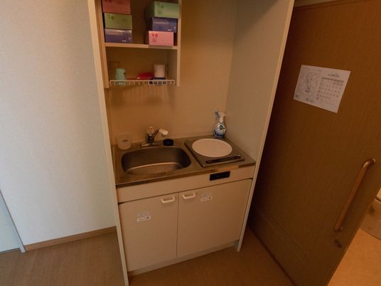 施設の写真 少し小さめの台所スペース。IH調理器具とシンクが設置されていて、シンクの上には洗い物を置く棚がある。