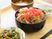サムネイル 黒い器に紅生姜ののった牛丼が盛られている。また、野菜系の小鉢が二種あり、手前には黒い箸が用意されている。