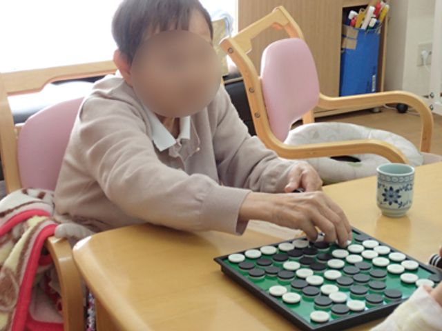 テーブルで遊ぶ人 ラウンジ 日差しが差し込む部屋で、ボードゲームを楽しむ利用者様のリラックスタイムが伺えます。穏やかなひとときを共有する空間です。