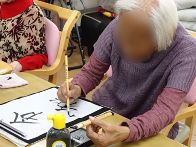 書道を楽しむ様子の多目的室 多目的室 書道を楽しむ入居者の姿が見られます。趣味を共有しながら交流する機会となっています。