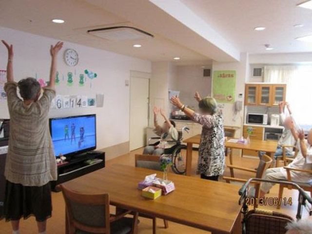 運動する高齢者の居室 レクリエーション 天気の良い日は、居室でリズム体操を通じて心身の健康をサポートします。楽しげな表情で体を動かす利用者様の姿が印象的です。