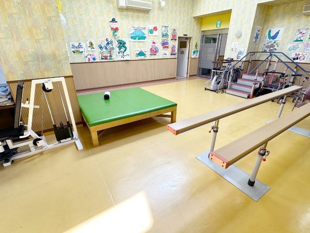 機能訓練室の一角 機能訓練室 明るい雰囲気の中で、運動やリハビリに集中できるスペースとなっています。壁には様々な作品が飾られています。