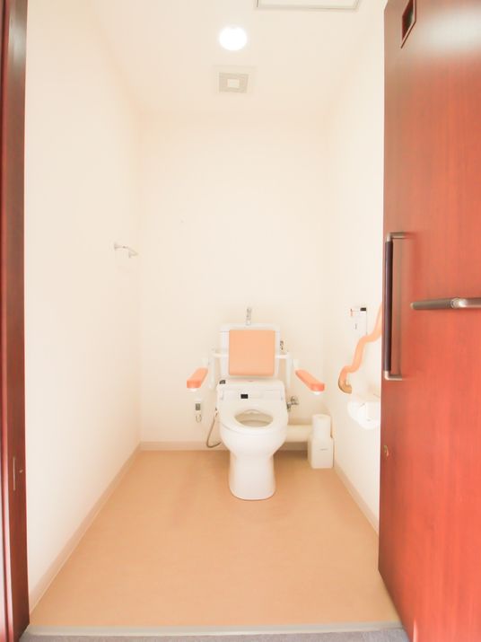 トイレは間口も奥行きも広く、床はフラットで移動もかんたん。壁には手すり、便座には背もたれがあるので安心して利用できる。