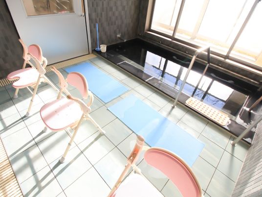 洗い場にシャワー椅子が3脚並べられている。窓の近くに大きな湯舟があり、出入り口には手すりが設けられている。