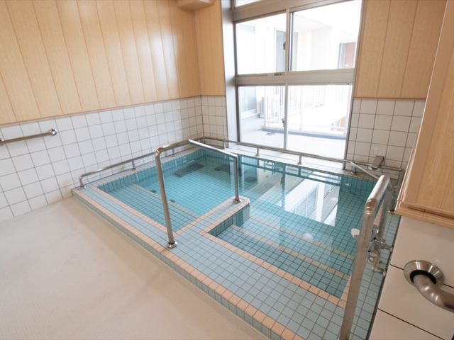 清潔な浴室の一角 大浴場 床面と壁の色彩が落ち着いた雰囲気を醸し出しており、手すりや広々としたスペースが安全に配慮されています。