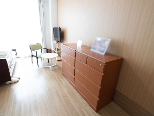 明るい居室の一角 収納家具 ゆったりとした広さの居室では、個々の生活スタイルに合わせた家具配置が可能です。窓から自然光が差し込み、心地よい時間を過ごせます。