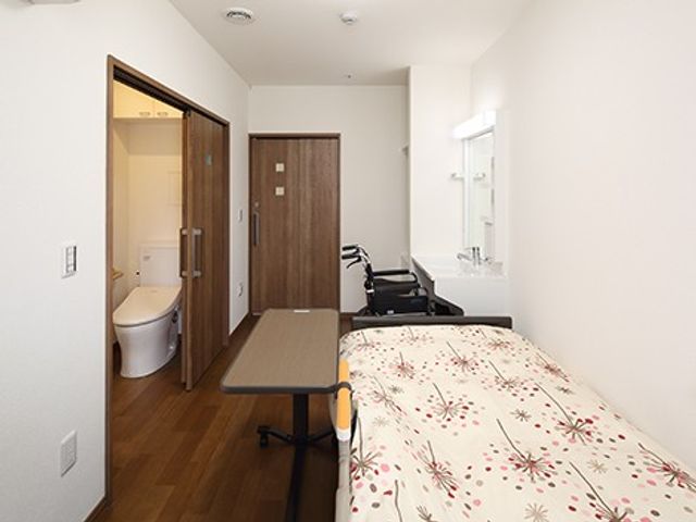 明るい居室の一角とトイレが見える居室 居室   ベッドと車椅子が置かれた、すっきりした居室です。廊下側にトイレが近く、移動のしやすさがうかがえます。