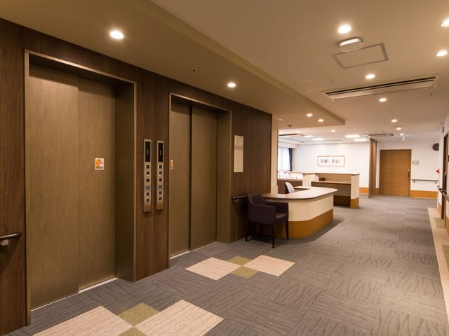 明るいロビーの全景 エレベーター ゆとりのある空間で、暖かな色合いで統一されたエントランスです。受付カウンターがあり、訪れる方を温かく迎えます。