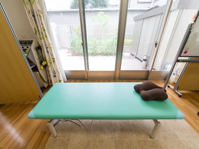 リハビリ用ベッドと緑の庭 室内 開放感のある明るい部屋でリハビリが可能です。窓越しには心安らぐ緑が見えます。